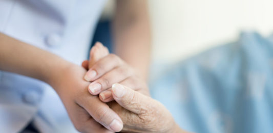 Une main de soignant serre la main d'une personne âgée