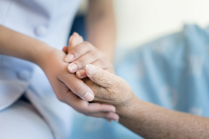 Une main de soignant serre la main d'une personne âgée