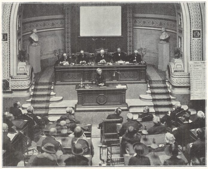 En 1925, dans l’amphithéâtre de l’Académie de médecine, Marie Curie, installée au pupitre, donne une conférence sur la radioactivité. © L'ILLUSTRATION