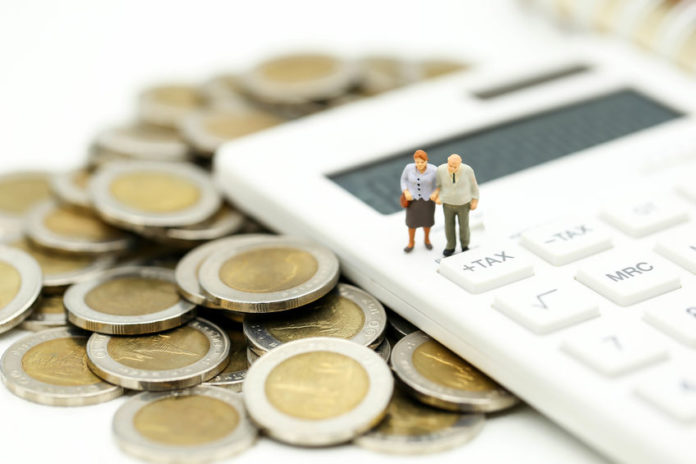 Figurine d'un couple de personnes âgées sur une calculette entourée de pièces d'euros