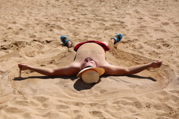 Homme couché sur le dos sur une plage en plein soleil