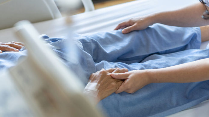 Patient âgé sur un lit d'hôpital, une infirmière lui tient la main
