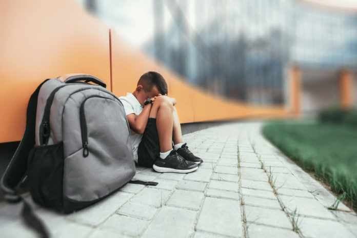 un enfant dépressif assis par terre avec un sac d'école posé à terre en premier plan
