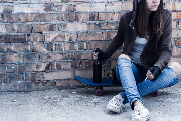 Jeune fille assise sur un skate entrain de fumer et boire