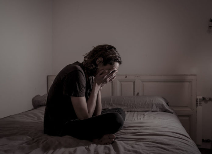 Desperate lonely teenager man suffering from depression sitting alone on bed